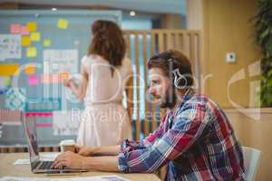 Male graphic designer listening song while using laptop