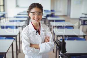 Portrait of schoolgirl standing with arms crossed in classroom