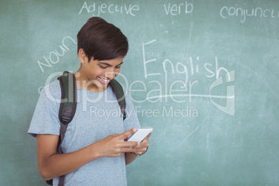 Happy schoolboy with backpack using mobile phone in classroom