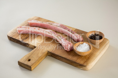 Sirloin chops, salt and black pepper on wooden board against white background