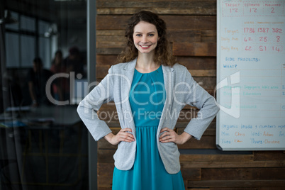 Smiling female business executive standing with hand on hip in office