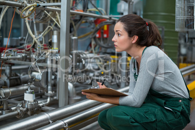 Female factory worker maintaining record on clipboard in factory