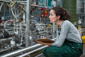 Female factory worker maintaining record on clipboard in factory