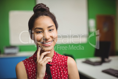 Portrait of smiling schoolgirl standing with hand on chin in classroom