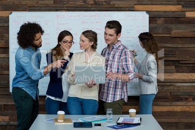 Business team discussing over laptop while colleague working in background