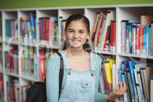 Portrait of happy schoolgirl selecting book in library