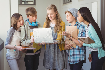 Smiling school students using laptop in corridor