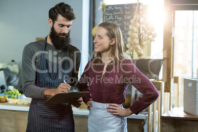 Smiling bakery staff writing on clipboard at counter