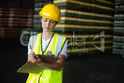 Female factory worker writing on clipboard in factory