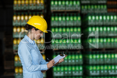 Female factory worker writing on clipboard in factory