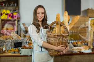 Portrait of smiling female staff holding a basket of baguettes at counter