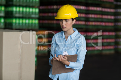 Female factory worker maintaining record on clipboard in factory