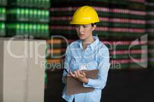 Female factory worker maintaining record on clipboard in factory