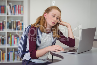 Thoughtful schoolgirl using laptop in library