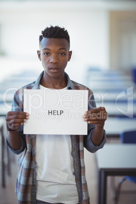 Schoolboy holding white paper with text sign in classroom
