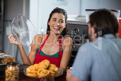 Smiling female staff serving bakery snacks to male customer at counter