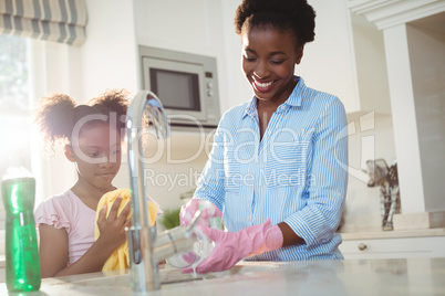 Mother assisting her daughter in cleaning utensils