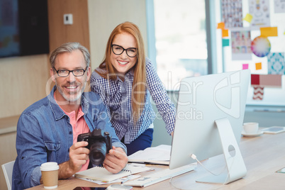 Portrait of male graphic designer holding digital camera with coworker