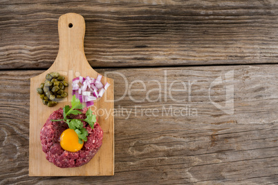 Minced meat with egg yolk, onions and olives on wooden tray