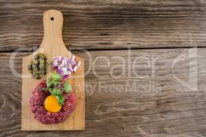 Minced meat with egg yolk, onions and olives on wooden tray