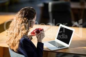 Female business executive looking at laptop while having cup of coffee