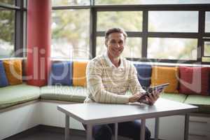 Portrait of happy school teacher using digital tablet in library
