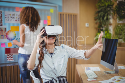 Female graphic designer using virtual reality headset with her colleague in background