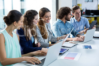 Smiling business team working on laptop and digital tablet in meeting