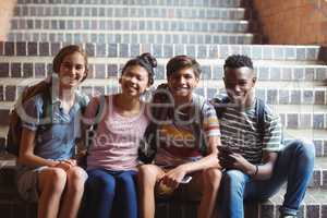 Portrait of happy classmates sitting on staircase