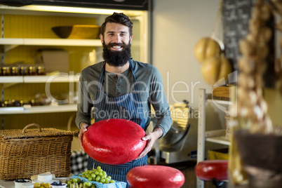 Smiling salesman holding a gouda cheese