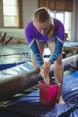 Female gymnast applying chalk powder on her hands before practicing