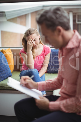 Sad schoolgirl sitting in library with teacher on foreground