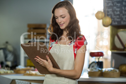 Female shop assistant writing on the clipboard at the counter