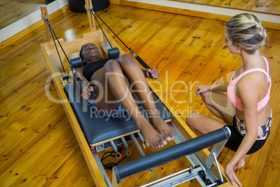 Trainer assisting woman with pilates on reformer