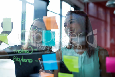 Business executives writing over sticky notes on glass