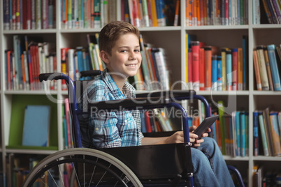 Portrait od disabled schoolboy holding digital tablet in library