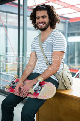 Smiling graphic designer sitting with skateboard in creative office