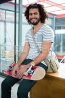 Smiling graphic designer sitting with skateboard in creative office