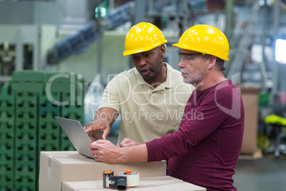 Factory workers discussing while working on laptop in drinks production plant
