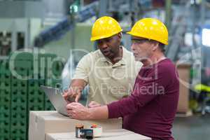 Factory workers discussing while working on laptop in drinks production plant