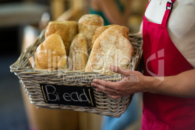 Mid section of male staff holding a basket of baguettes at counter