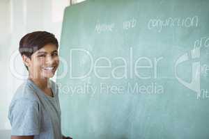 Portrait of smiling schoolboy standing near chalkboard in classroom