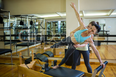 Female trainer assisting woman with stretching exercise on reformer