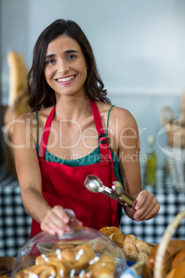 Portrait of smiling female staff holding tongs at counter