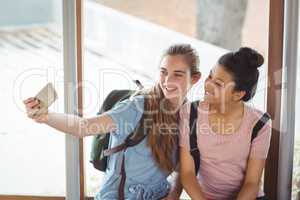 Happy schoolgirls taking selfie on mobile phone in corridor