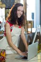 Female shop assistant using laptop at the counter in grocery shop