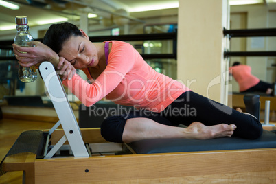 Tiered woman holding water bottle and relaxing on reformer