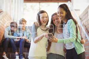 Smiling schoolgirls using mobile phone in corridor