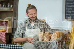 Smiling male staff holding a basket of baguettes at counter