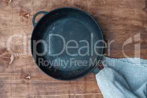 Black cast-iron empty frying pan on a brown wooden surface